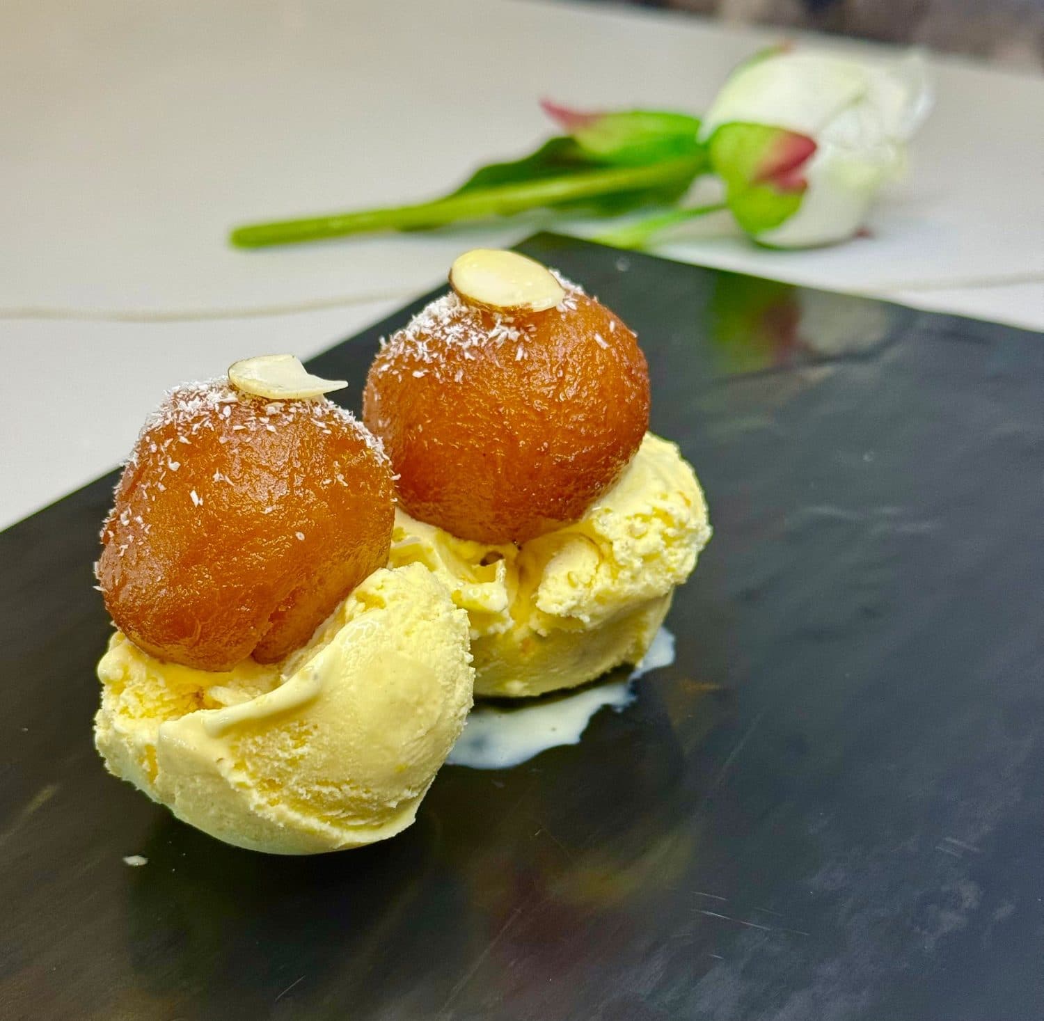 Gulab jamun served over pistachio kulfi ice cream, garnished with sliced almonds