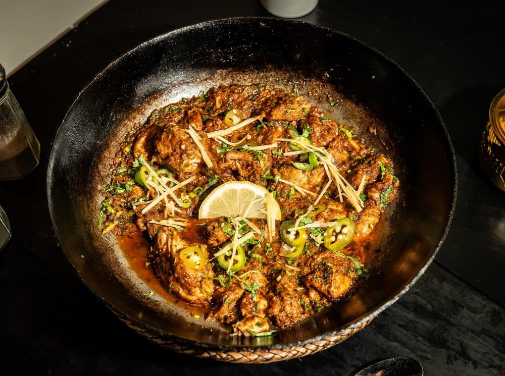 Lahori chicken karahi in a cast iron karahi, garnished with lemon, ginger and green chilies