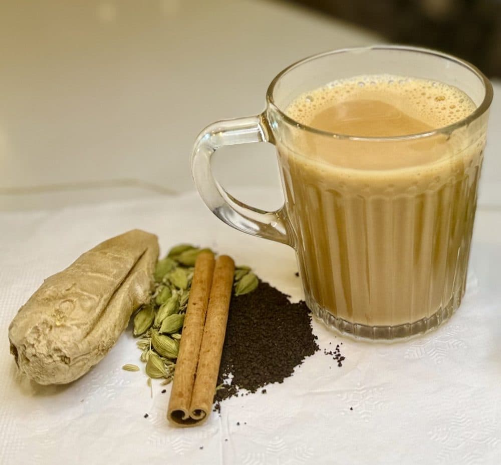 A mug of masala chai beside whole spices — cardamom, cinnamon, ginger and loose tea